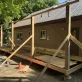 A house under construction with a brown exterior and a gray metal roof, with new wooden deck framing and subflooring.